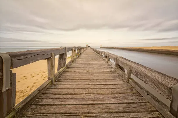 Long ponton en bois sur la plage menant vers l'océan sous un ciel nuageux.