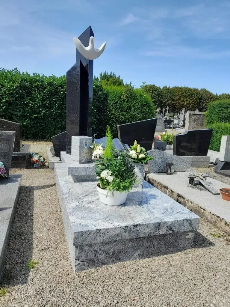 Monument funéraire moderne en granit gris clair avec sculpture d'oiseau blanc.
