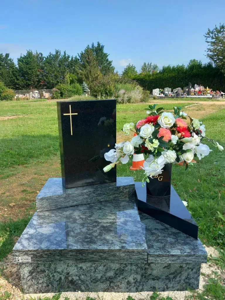 Petit monument cinéraire sombre avec stele en granit noir et bouquet de fleurs.