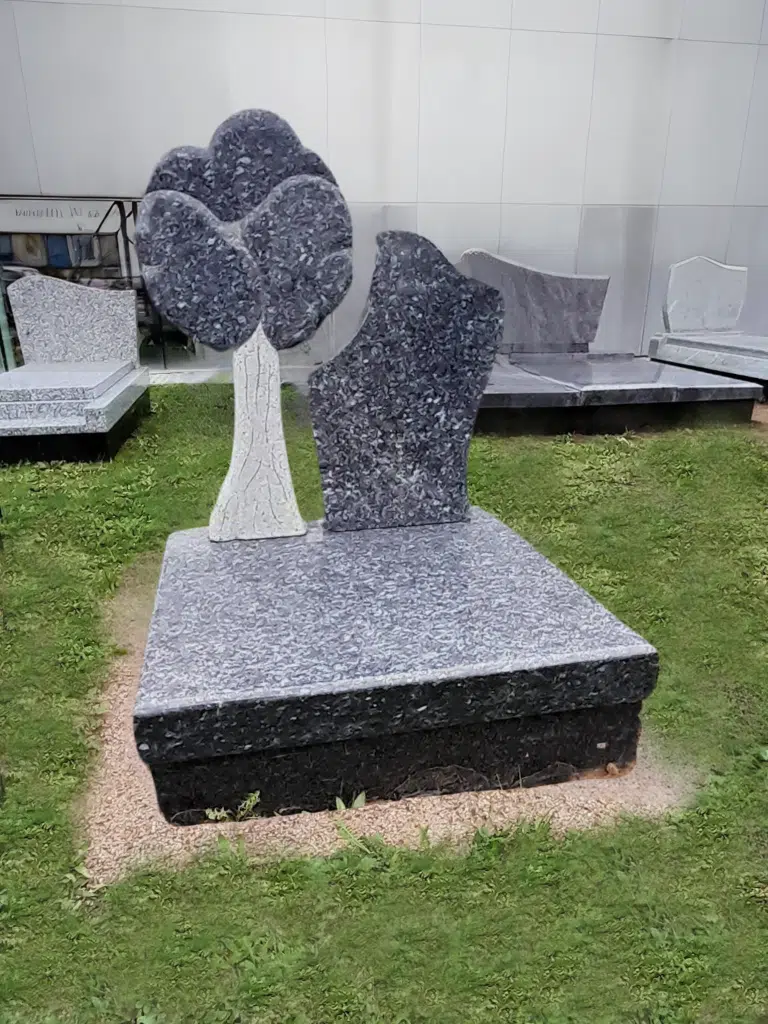 Monument cinéraire original en granit gris avec sculpture d'arbre.