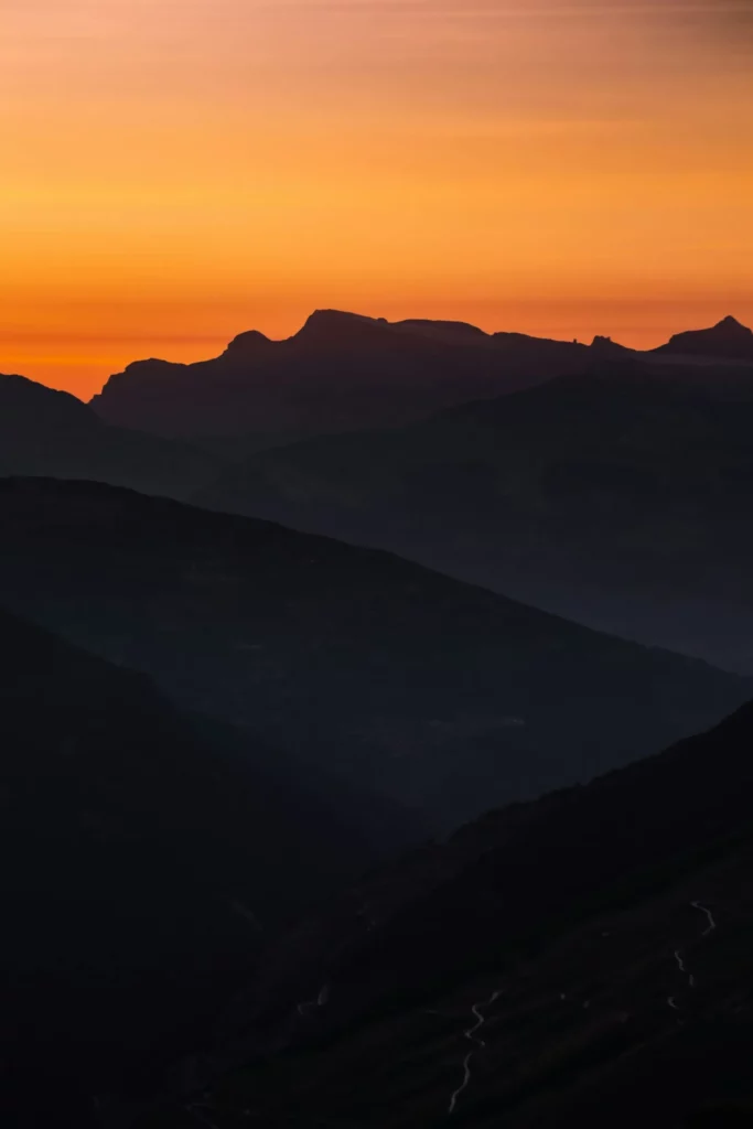 Silhouettes de chaînes de montagnes sombres se découpant sur un ciel orange et jaune.