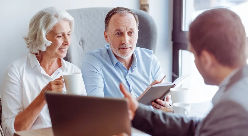 Couple senior souriant et discutant avec un conseiller financier lors d'un rendez-vous.