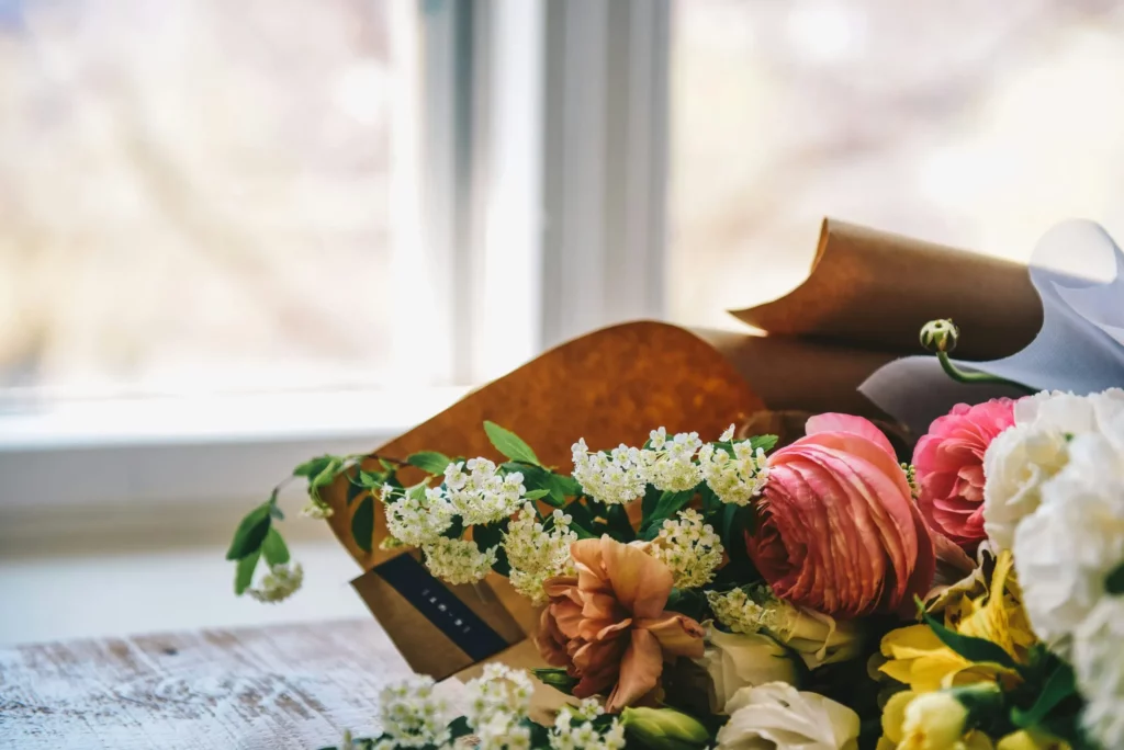 Proche d'un bouquet de mariée aux fleurs roses, blanches et jaunes sur une table en bois.